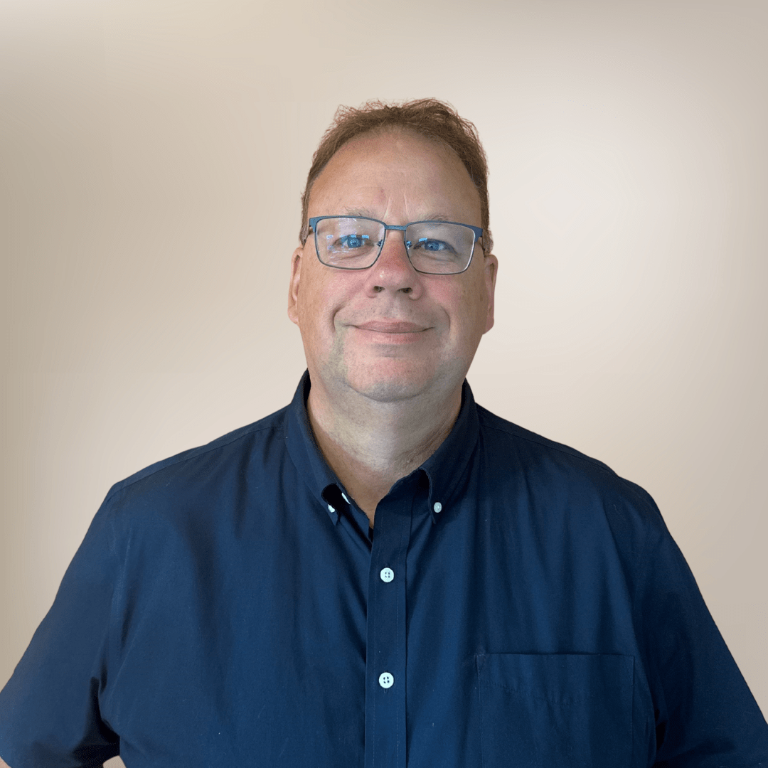Smiling man in dark blue shirt, neutral background.